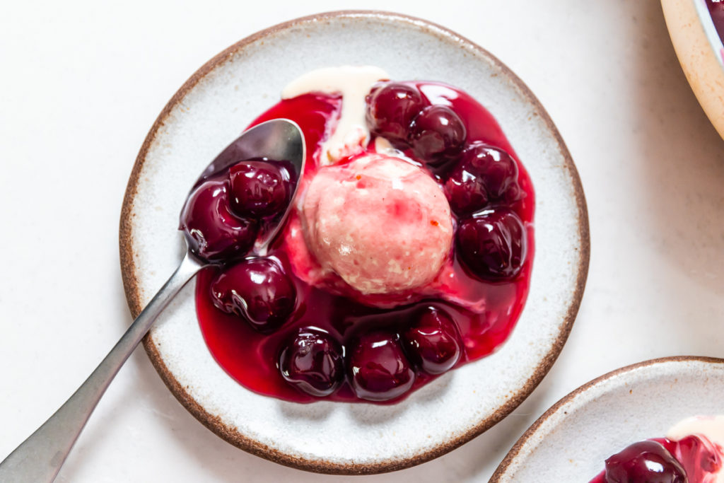 a plate with warm, gooey red cherries jubilee over a scoop of vanilla ice cream